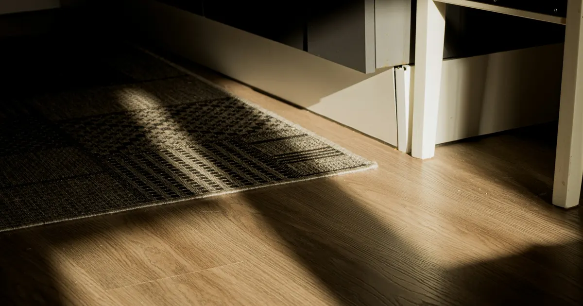 Close view of plank flooring with a rug edge and soft daylight