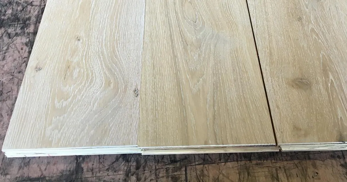 Three wide oak planks side by side, showing knots and open grain, with the layered edge of an engineered board at the bottom