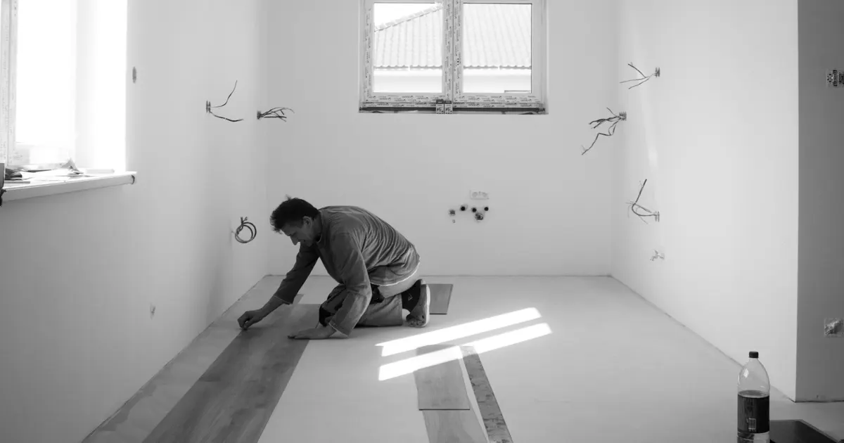 Installer kneeling on a bare floor laying wood boards in an empty room